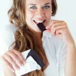 Portrait of young woman in underwear eating chocolate. Isolated on white.