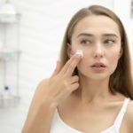 Young beautiful woman applying cream to face in the bathroom